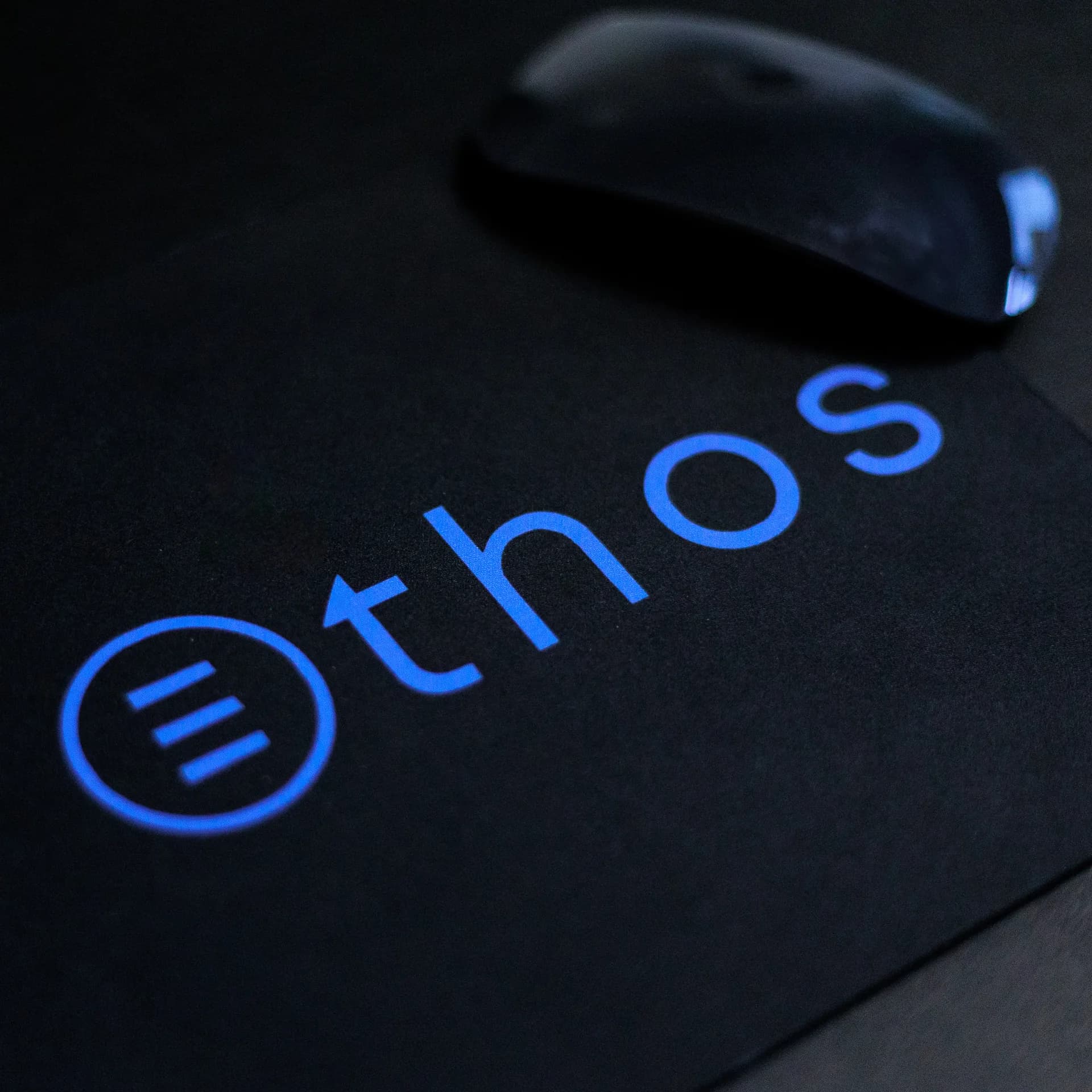 Blue Ethos wordmark on a black desk mat beside a mouse
